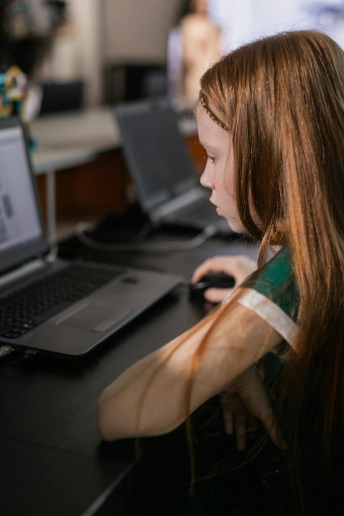 Young girl engaged in online learning using a laptop, focused on her studies in a modern setting.